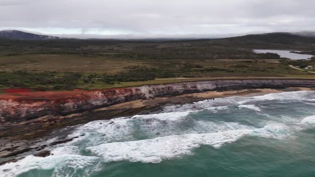 Aerial video flying over the rugged coastline at Lake Arragan, featuring sandy shoreline, rocky formations and waves rolling in from the Pacific Ocean