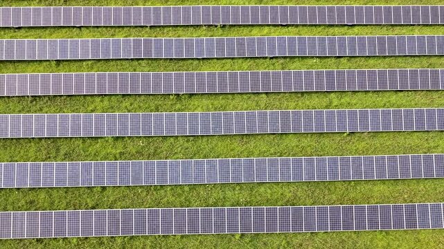 Rows of solar panels run in parallel lines across mown grass at a solar field in Patterson, New York, the array filling the frame from one edge to the other. Aerial top down