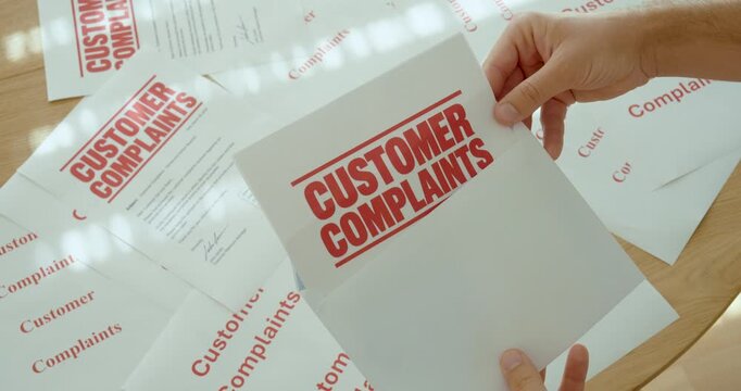 Close-up of hands holding a customer complaint document surrounded by multiple complaint forms, representing customer dissatisfaction and complaint management.