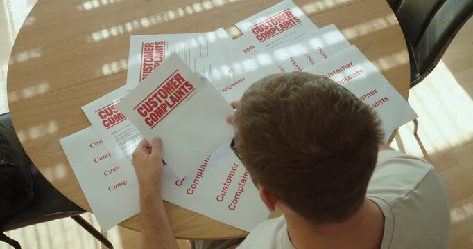 Overwhelmed man surrounded by multiple customer complaint documents, reviewing complaints and dealing with customer service issues.