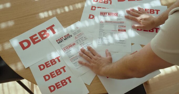 Close-up of man overwhelmed by multiple debt notices and overdue payment letters, showing financial stress and personal debt problems.