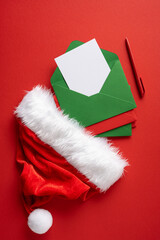 Naklejka premium Christmas letter to Santa with green envelope and red Santa hat on red vertical background