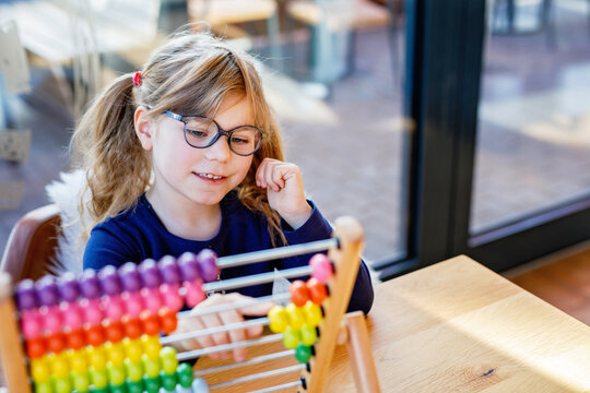 Little preschool girl playing with educational wooden rainbow toy counter abacus. Healthy happy child with glasses learning to count and colors, indoors on sunny day.