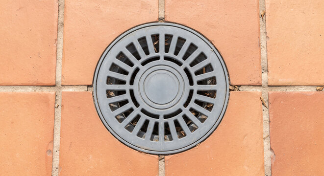Circular gray drainage cover on terracotta tiled floor in urban setting