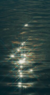 Sparkling reflections move across dark water. Rippling water shimmers with bright sunlight reflections in serene abstract view. Dark surface glows with moving highlights forming peaceful pattern.