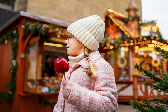 Little cute kid girl eat sweet sugar covered red candy apple on Christmas market. Happy child on traditional Xmas fair in Germany.