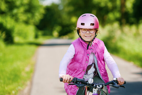 Young girl wearing eyeglasses and a helmet riding a bicycle on a quiet country road surrounded by green nature on a sunny day.