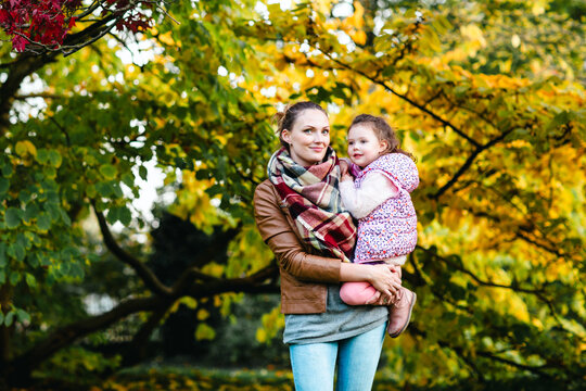Mother and daughter walking in autumn park together. Happy family enjoying fall season outdoors. Real life, real people