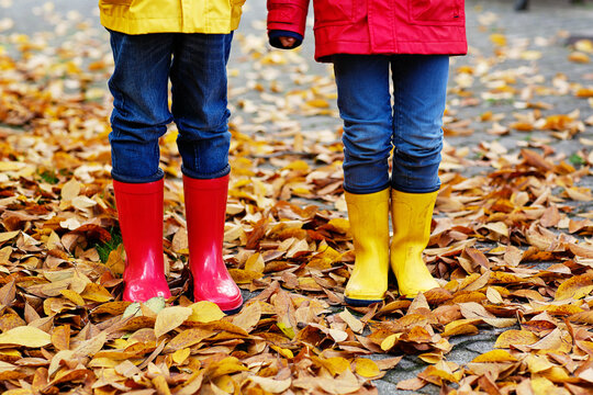 Closeup of kids legs in rubber boots dancing and walking through fall leaves