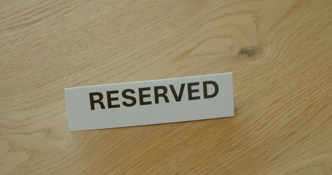 Close-up of hand placing a Reserved sign on a wooden table, representing table reservation, booking and reserved seating.