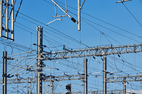 Railway catenary electrification and overhead line infrastructure with steel gantries, contact wires, insulators and traction power equipment, showing complex electric rail transport infrastructure