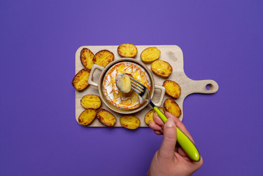 Fork lifting stretchy melted cheese from a baked camembert