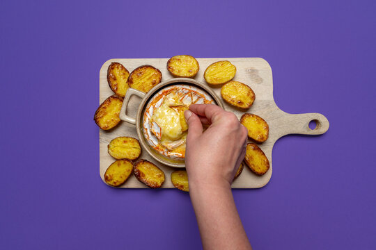Hand dipping a potato into melted baked camembert
