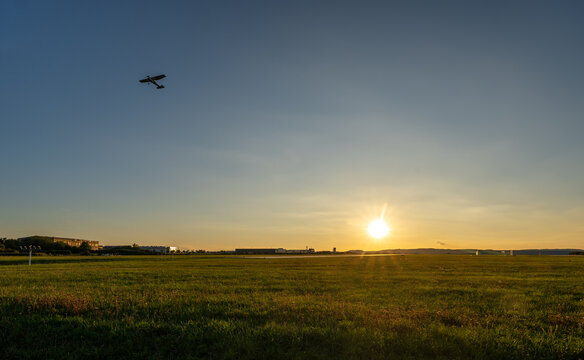 Small aircraft flying over an airfield at sunset