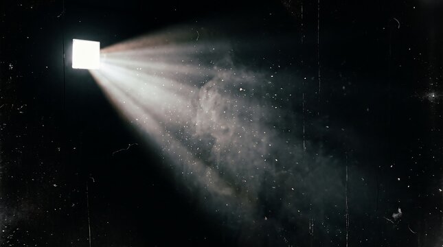 Light beam shining through a small opening creating dust particles in a dark space with bright light source