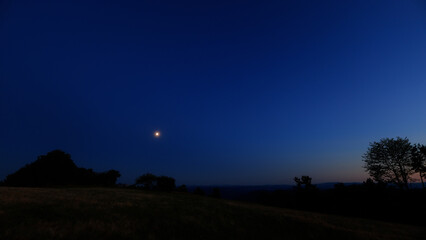 Moon on a twilight sky with stars, planets and landscape mountain silhouettes. © astrosystem