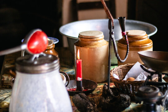 Vintage kitchen scene with ceramic jars, burning red candle, woven basket, and old utensils on table