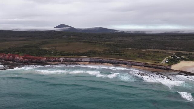 Aerial video flying over the rugged coastline at Lake Arragan, featuring sandy shoreline, rocky formations and waves rolling in from the Pacific Ocean