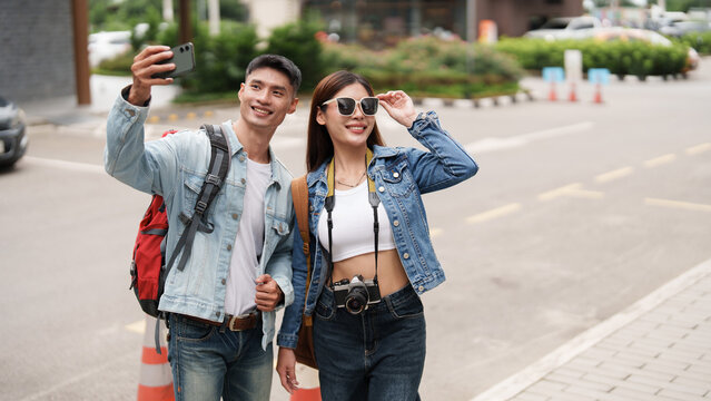 Asian tourist couple taking selfie with smartphone while exploring city on travel trip