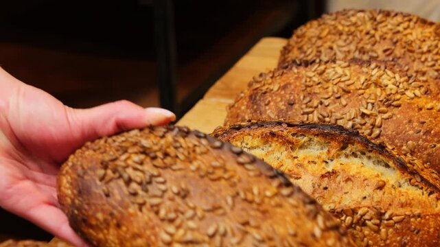 Shop assistant arranges bread with various nutritious seeds on counter. Fragrant bread topped with sesame sunflower and pumpking seeds