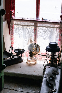 Rustic interior still life featuring antique kerosene lamps, balance scales, and suitcase near window