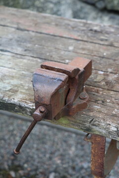 Rusty vise on a weathered wooden workbench outdoors, showing age, texture, and rugged industrial character.