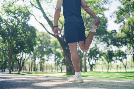 Rear view of athlete stretching quad muscle on park trail for fitness warmup routine