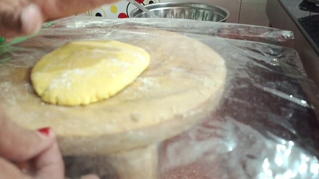 Indian woman kneading yellow corn flour dough and rolling makki roti on wooden board