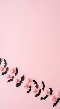 halloween decoration with black paper bats and pastel pink mini pumpkins on pink background, festive autumn mood