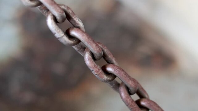 Panning shot of heavy rusty steel chain links hanging in workshop.