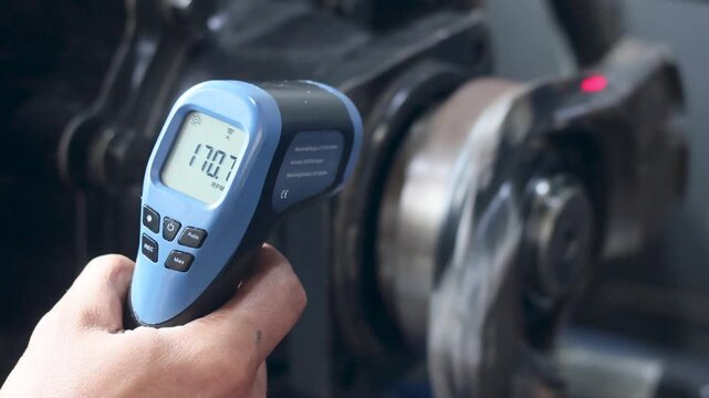 Panning shot of technician measuring machinery rotation using digital tachometer in workshop.