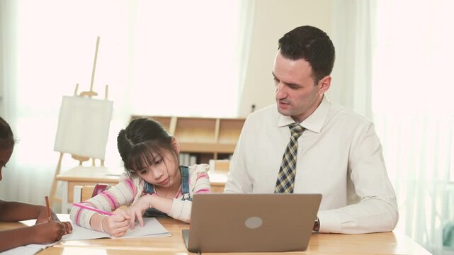 Male teacher helps elementary student during small group learning activity with laptop in classroom, supporting individual guidance, digital education, student development.