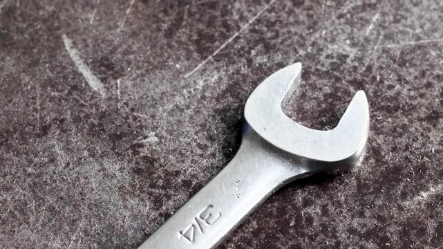 Panning shot of open end spanner wrench resting on metal workshop table.