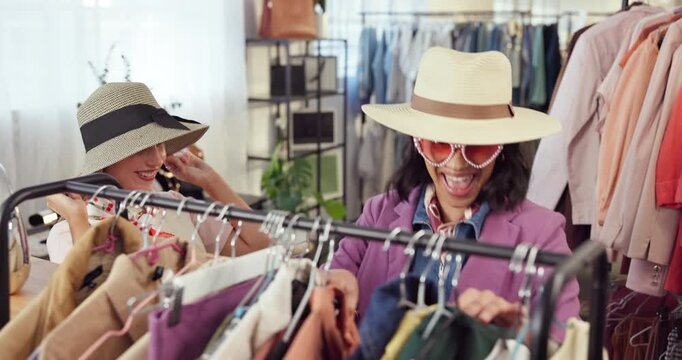 Fashion, shopping and woman with friends for fitting, playful or excited with choice in store. Happy people, boutique and try clothes with stylish hat at rack for fun, talk and wow with customer deal