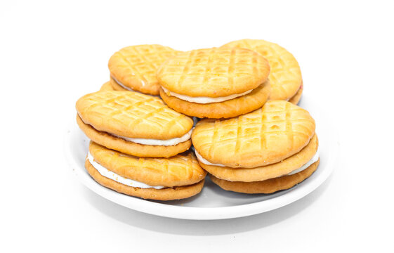 Stack of biscuits with sweet cream strawberry jam filling on a white plate isolated on white background. Golden round cream sandwich with strawberry jam inside