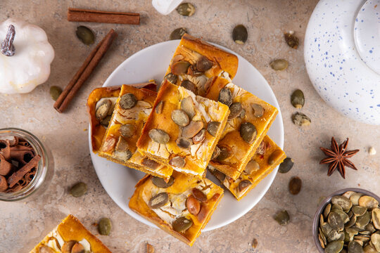 Sweet autumn baking recipe, pumpkin cream cheese brownies. Marbled pumpkin and cheesecake brownie bars on beige concrete background