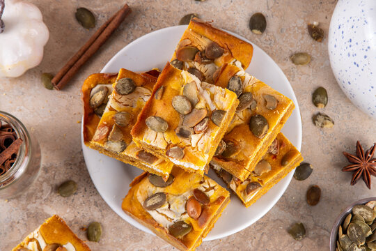 Sweet autumn baking recipe, pumpkin cream cheese brownies. Marbled pumpkin and cheesecake brownie bars on beige concrete background