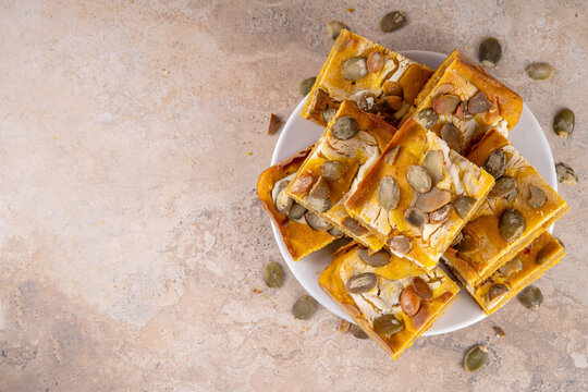 Sweet autumn baking recipe, pumpkin cream cheese brownies. Marbled pumpkin and cheesecake brownie bars on beige concrete background