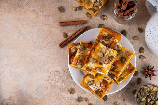 Sweet autumn baking recipe, pumpkin cream cheese brownies. Marbled pumpkin and cheesecake brownie bars on beige concrete background