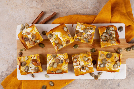 Sweet autumn baking recipe, pumpkin cream cheese brownies. Marbled pumpkin and cheesecake brownie bars on beige concrete background