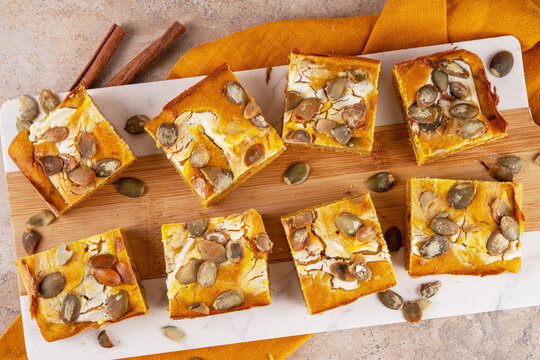 Sweet autumn baking recipe, pumpkin cream cheese brownies. Marbled pumpkin and cheesecake brownie bars on beige concrete background