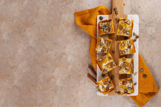 Sweet autumn baking recipe, pumpkin cream cheese brownies. Marbled pumpkin and cheesecake brownie bars on beige concrete background