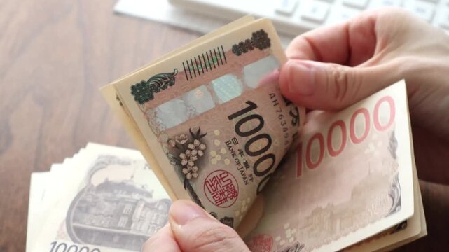 木製テーブルで紙幣を数える女性の手のアップと机上の電卓