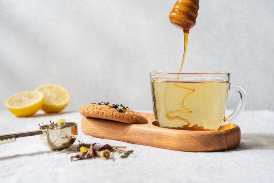 Warm tea with honey dripping from a wooden dipper into a transparent glass mug, cozy homemade beverage concept