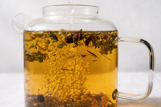 Close up of herbal tea brewing in a transparent glass teapot on a light background, natural warm beverage concept