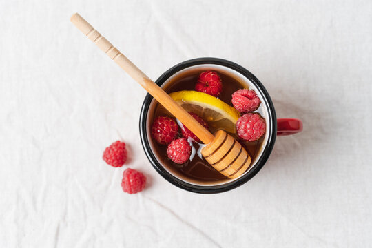 Raspberry tea with lemon and honey served in a red mug on a table, warm homemade beverage for cozy autumn and winter days