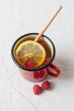 Raspberry tea with lemon and honey served in a red mug on a table, warm homemade beverage for cozy autumn and winter days