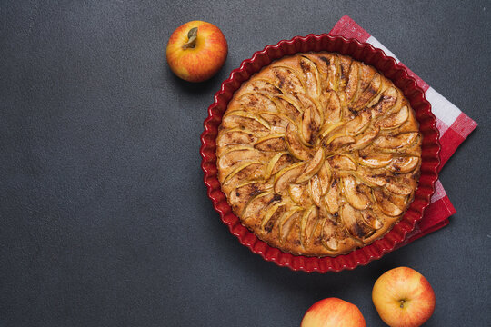 Homemade apple pie baked in a red ceramic dish on a dark background, rustic seasonal dessert for cozy autumn and holiday baking