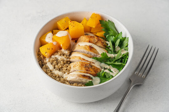 Autumn quinoa bowl with roasted pumpkin, chicken breast and fresh parsley in a bowl on a light background, healthy homemade seasonal meal