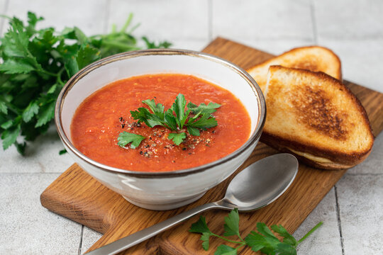 Homemade tomato soup with crispy cheesy toasts served on a light kitchen table, comforting warm meal concept for cozy autumn and winter dining, healthy homemade comfort food